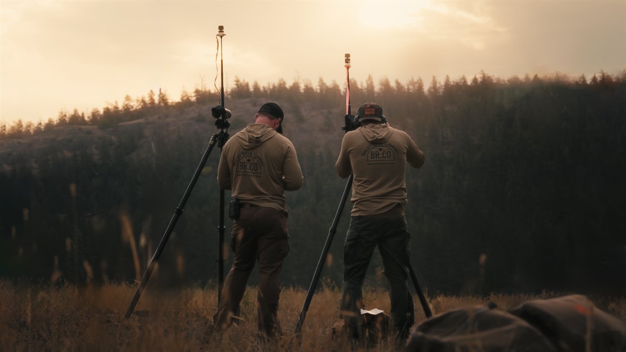 Two people in Bagley Rifle Company apparel outdoors at sunset